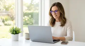 A woman in glasses working on her laptop on her desk at home.