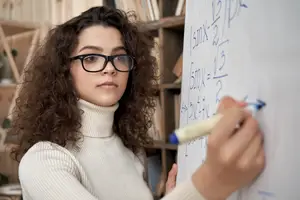 A girl is writing on a whiteboard with mathematical equations and expressions