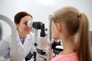 A woman is looking through a microscope at a young girl who is looking at the camera