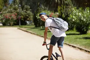 A man is riding a bicycle on a pathway with green grass and trees on the side.