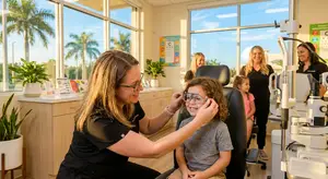A woman helps a child try on glasses in a well-lit optometrist's office.