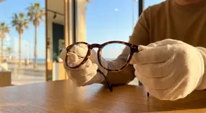 A person wearing gloves is holding a pair of eyeglasses on a table.