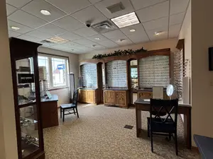A photo of an interior of an establishment that seems to be a shop for eyeglasses with a desk, chairs, and glass cabinets with eyeglasses on display.