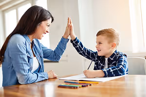 A woman and a boy are doing a high-five on a table with papers and crayons.