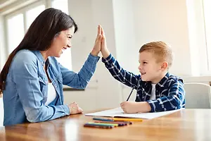 A woman and a boy are doing a high-five on a table with papers and crayons.