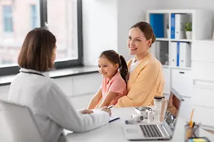 A woman doctor with a young girl patient and mother in an office