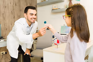 A man in a white coat is showing a girl a lollipop and a globe