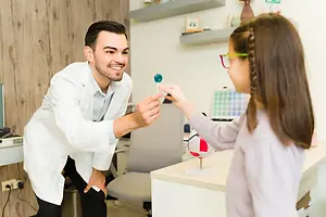 A man in a white coat is showing a girl a lollipop and a globe