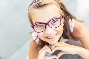 A smiling girl with braces and glasses posing for a photo.