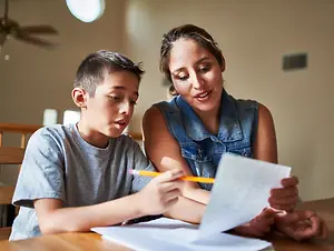 A mother helping her son with his homework in a dining room