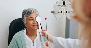 An older woman having her eye examined by a doctor using a phoropter and a red light.