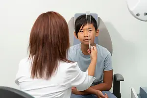 A young boy is having his eyes examined by a doctor in a medical setting.
