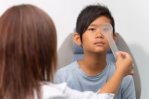 A boy with a doctor examining his eye with a plastic spoon.