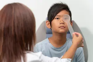 A boy with a doctor examining his eye with a plastic spoon.