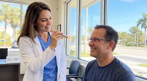 A woman holding a device is smiling at a man in a clinic.