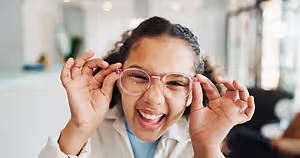 A young girl wearing glasses and smiling while looking at something