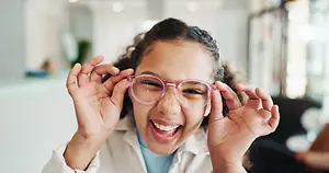 A young girl wearing glasses and smiling while looking at something
