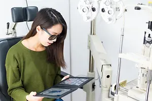 A woman with glasses looking at a tablet in an eye clinic