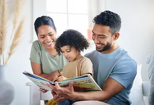 A family with a child is sitting on a couch and reading a book together