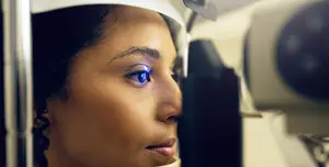 A woman with blue eyes is looking at something in front of her while wearing a white headband and a machine that is probably used for checking her eyesight.