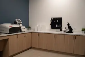 A modern office space with white walls and wooden cabinets and equipment on the counter.
