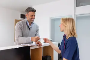 A man and a woman are smiling and interacting with each other in a room with white walls and wooden furniture.