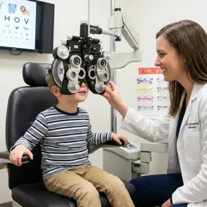 A young boy is sitting in an eye doctor's chair while a woman is examining his eyes.