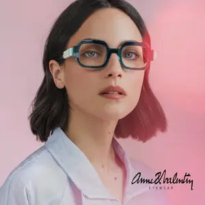 A woman wearing Anne & Valentiny eyeglasses poses in front of a pink background