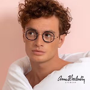 A man with curly hair wearing Anne and Valentin Eyewear glasses and a white shirt