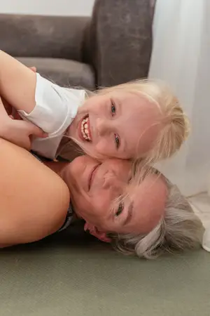 A woman lying on the floor with a little girl sitting on her back and smiling while looking at the camera