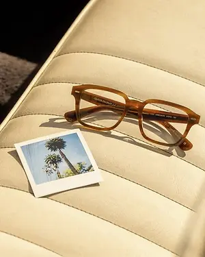 An image of glasses and a Polaroid picture sitting on a white leather seat cushion