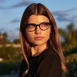 Close up of a woman with long hair and glasses standing in an outdoor setting