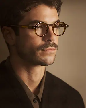 A man with a mustache wearing glasses is posing for a picture with a serious expression.