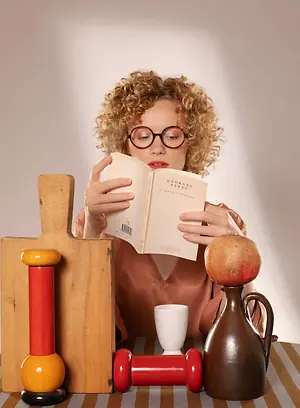 A woman reading a book about Georges Perec with various objects on a table.