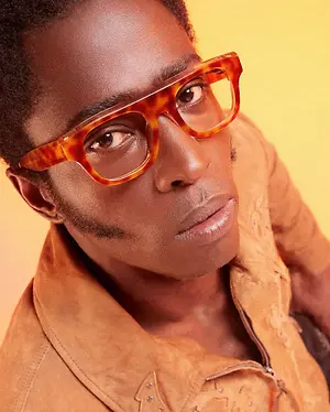 A man with glasses and a brown jacket posing for a picture