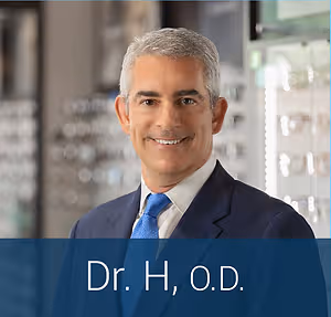 Dr. H, O.D. smiles in a suit at an optometrist's office