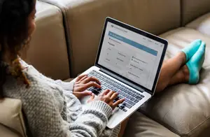 A woman sitting on a couch is working on a laptop computer.