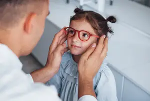 A man is examining a little girl's eyes with a red-framed spectacle