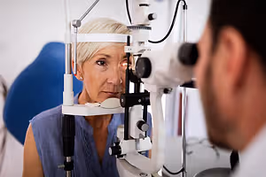 An older woman with short blonde hair is getting her eyes examined by an optometrist in an eye clinic.