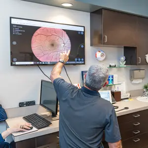 A man pointing at a monitor with an image of a retina on it in a medical office