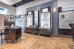 A room with wooden flooring and a monitor on a desk, there are cabinets, glass cabinets with different kinds of eyeglasses, and a surveillance camera on the ceiling.