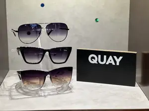 Three pairs of Quay sunglasses are displayed on a clear holder next to a black box with the word Quay on it.