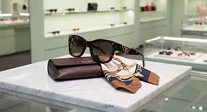 Accessories including sunglasses, a scarf, and a leather case are displayed on a marble table in a store.