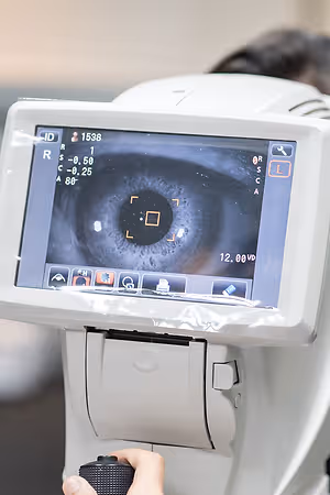 A white machine with a digital screen displaying an eye image is being held by a person with their right hand.