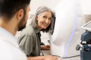 An older woman with gray hair is getting her eye examined by a man wearing a white coat in a medical office.