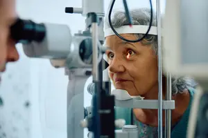 An elderly woman having her eye examined by an optometrist with a slit lamp