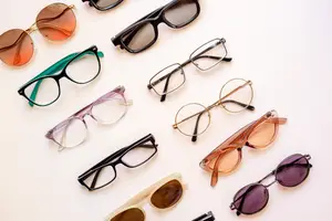 Multiple pairs of glasses are arranged on a white surface, including round, square, and oval frames in various colors and styles.