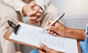 A healthcare provider is completing a patient form while another individual is sitting behind them.