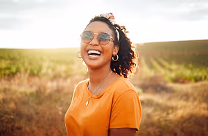 A woman smiling and laughing while standing in a field with dry grass