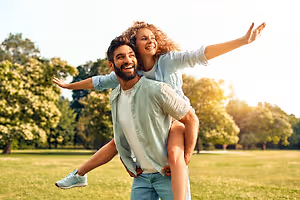 A couple playing in a park with the woman sitting on the man's shoulders